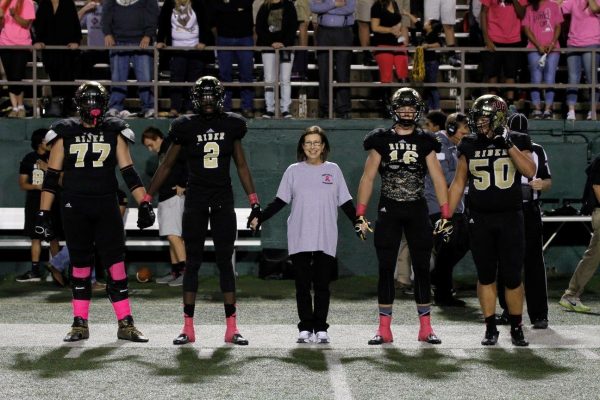 Jan Albin (center) walks out with Rider football captains before an October 2015 game where the Raiders wore pink for Breast Cancer Awareness.